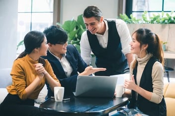a group of people sitting around a table with a laptop. 