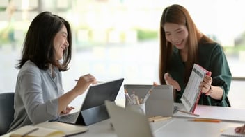 a couple of women sitting at a table with laptops.